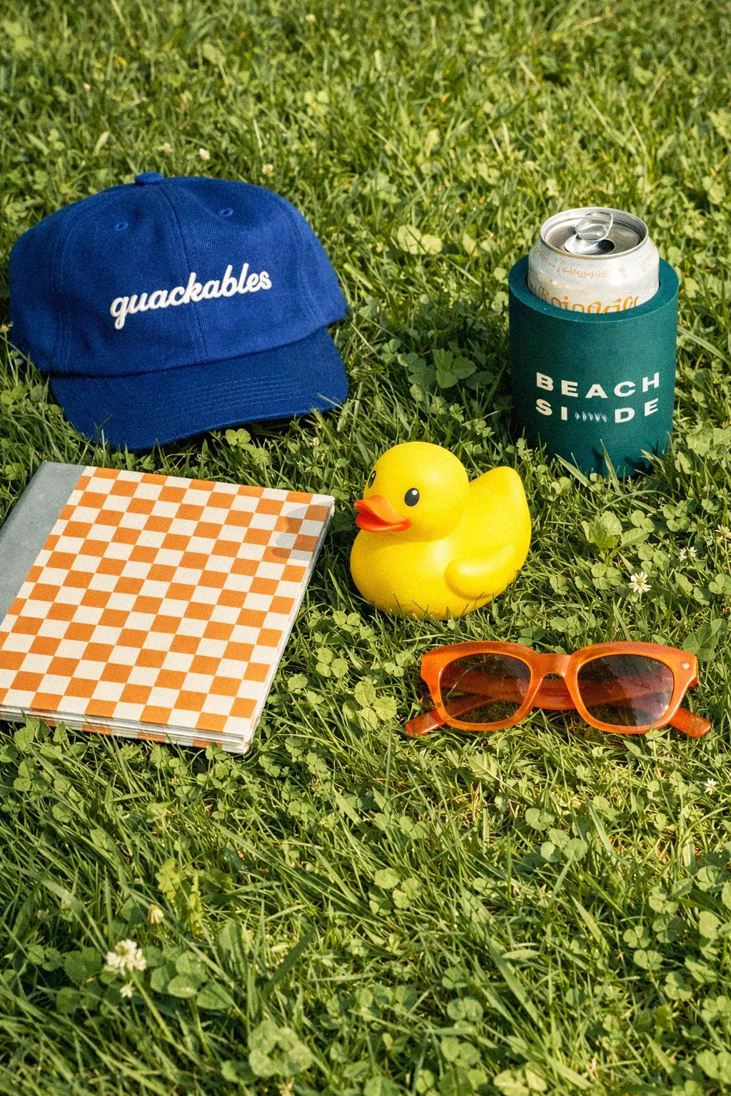 Quackables — flatlay na travi sa kačketom, patkom, naočarima i limenkom